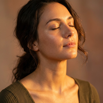Woman with closed eyes and peaceful expression in warm golden light representing wellness and recovery