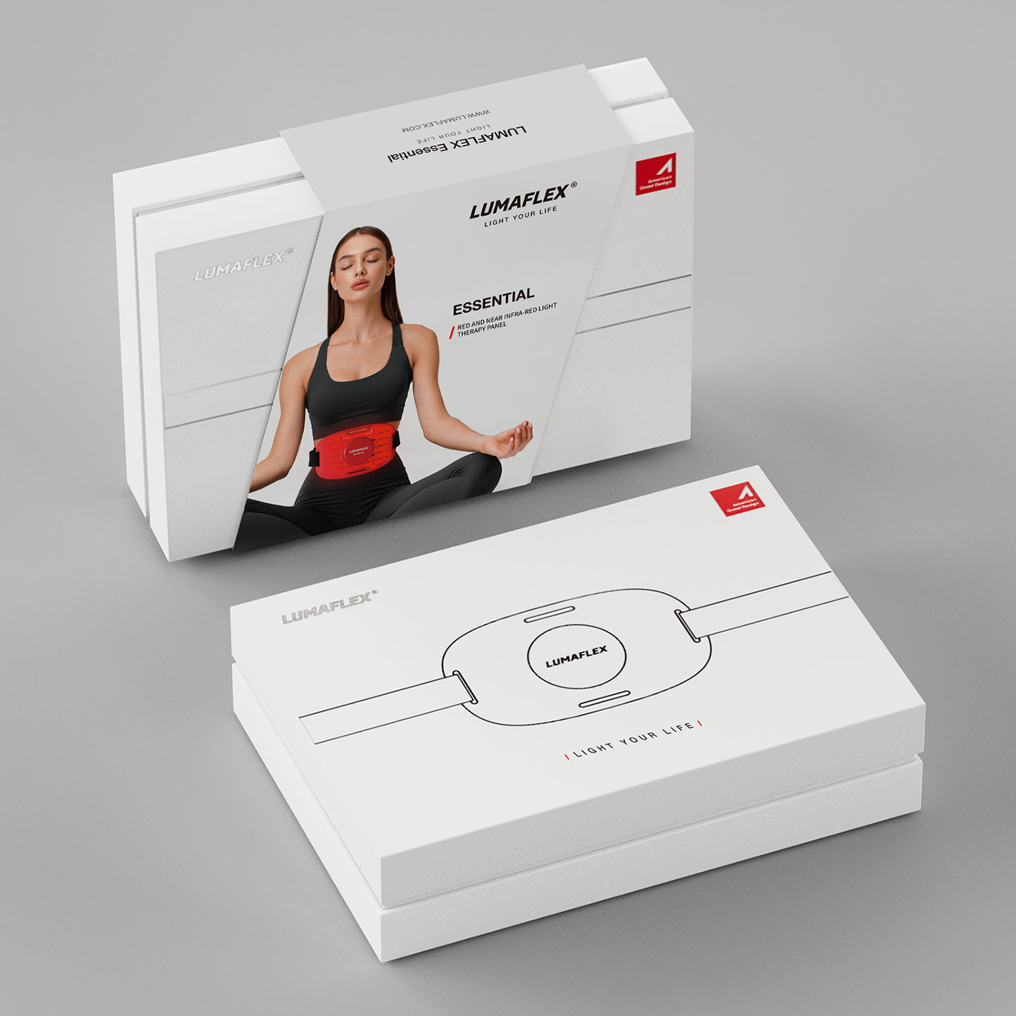Two white Lumaflex Essential lumbar support product boxes on a clean light gray studio background. The front box shows the lumbar support device illustration and the brand name, while the rear box displays a model wearing the red lumbar support belt.